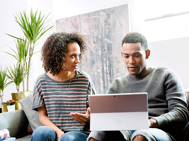 Man and woman seated on a sofa use a laptop to sign in securely to a federated identity provider.